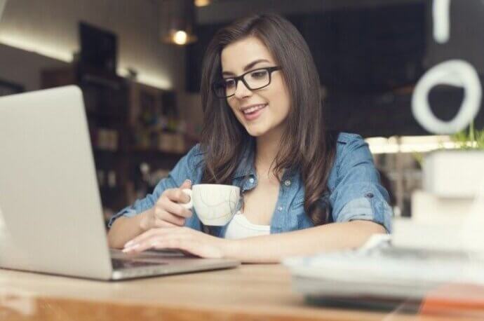 девушка с чашкой сидит перед ноутбуком